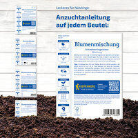 Anleitung für Blumensamenmischung in einer weißen Verpackung mit blauen Texten, auf Erde liegend.