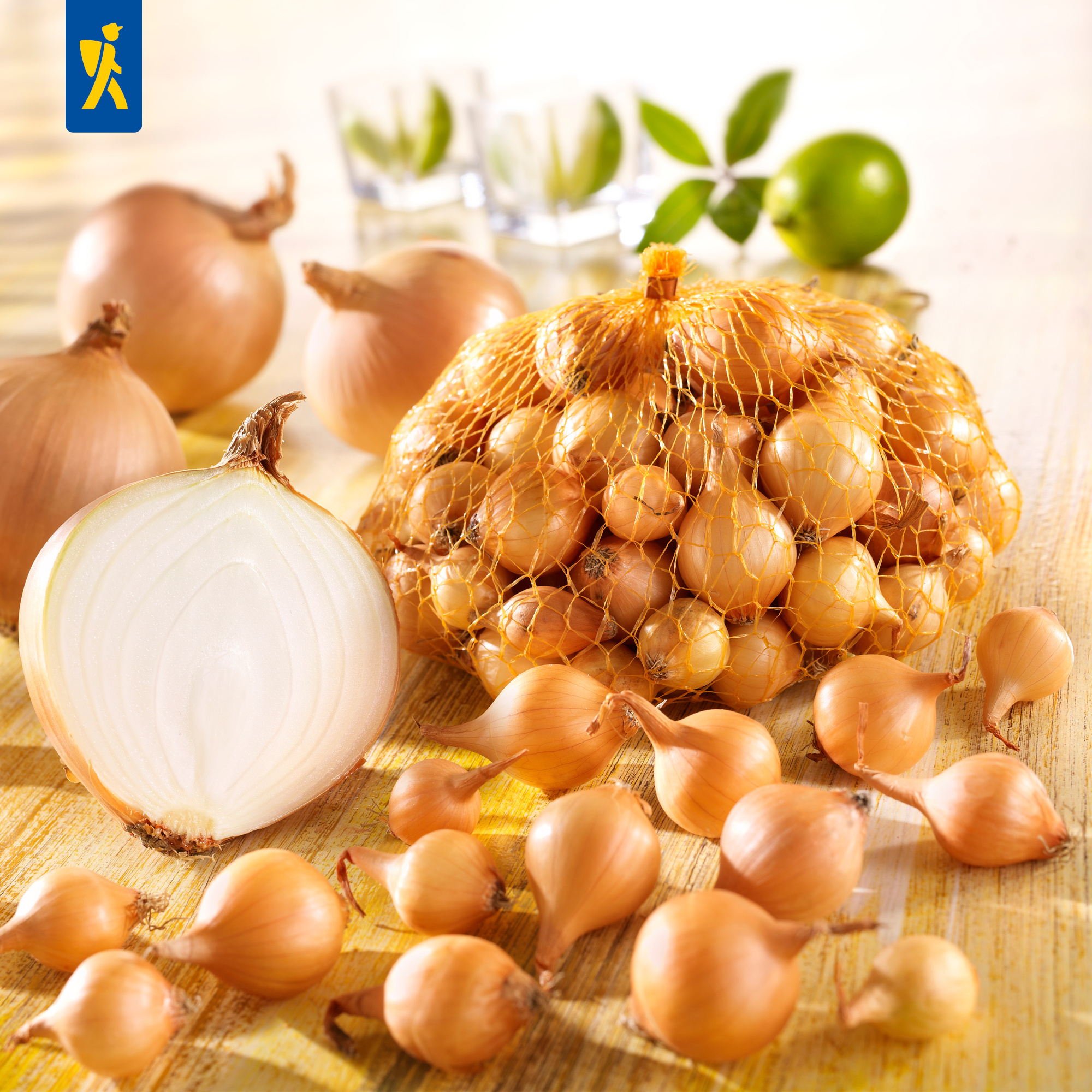 Zwiebeln in Netz, ganze Zwiebeln, halbierte Zwiebel, paar Gläser mit Zitronen, grüne Limette, grüne Blätter.