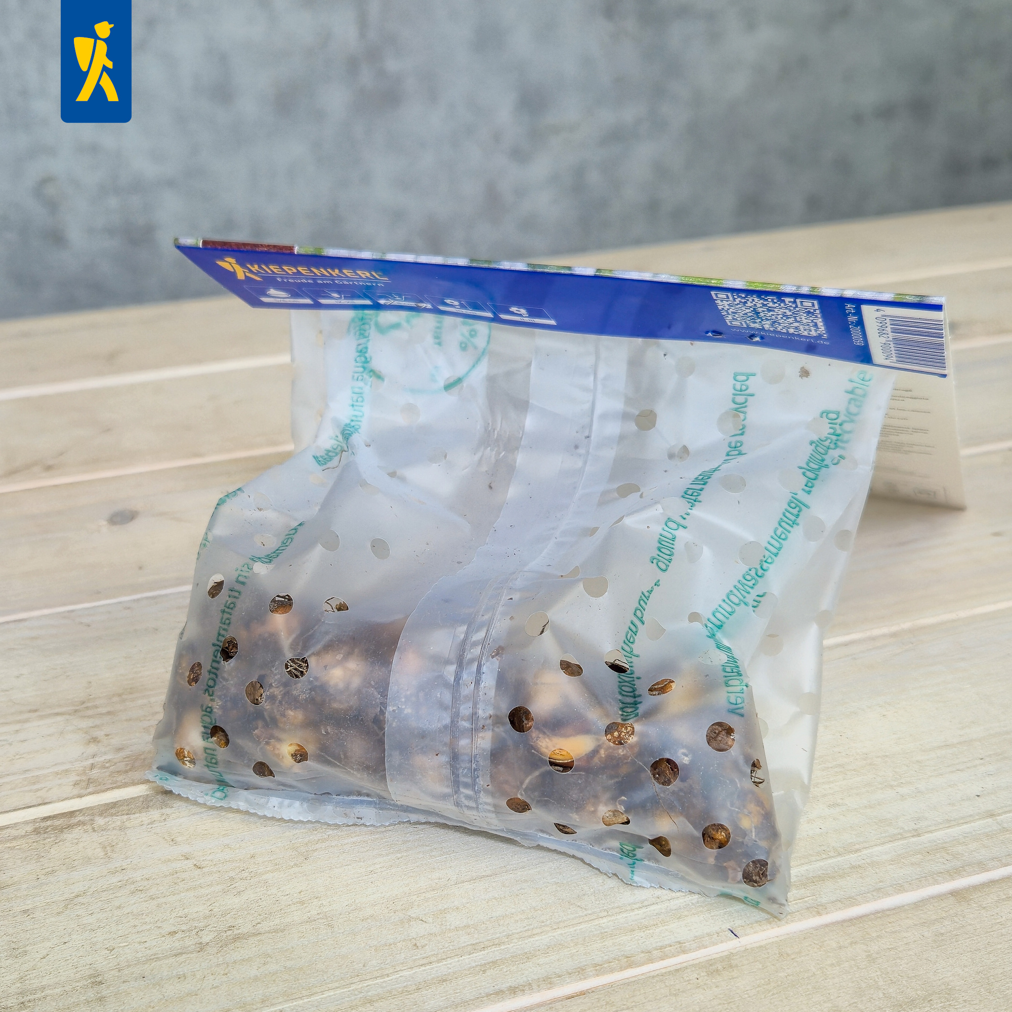 Leeres transparenter Beutel mit Löchern liegt auf Holzbank, blauer Karton oben.