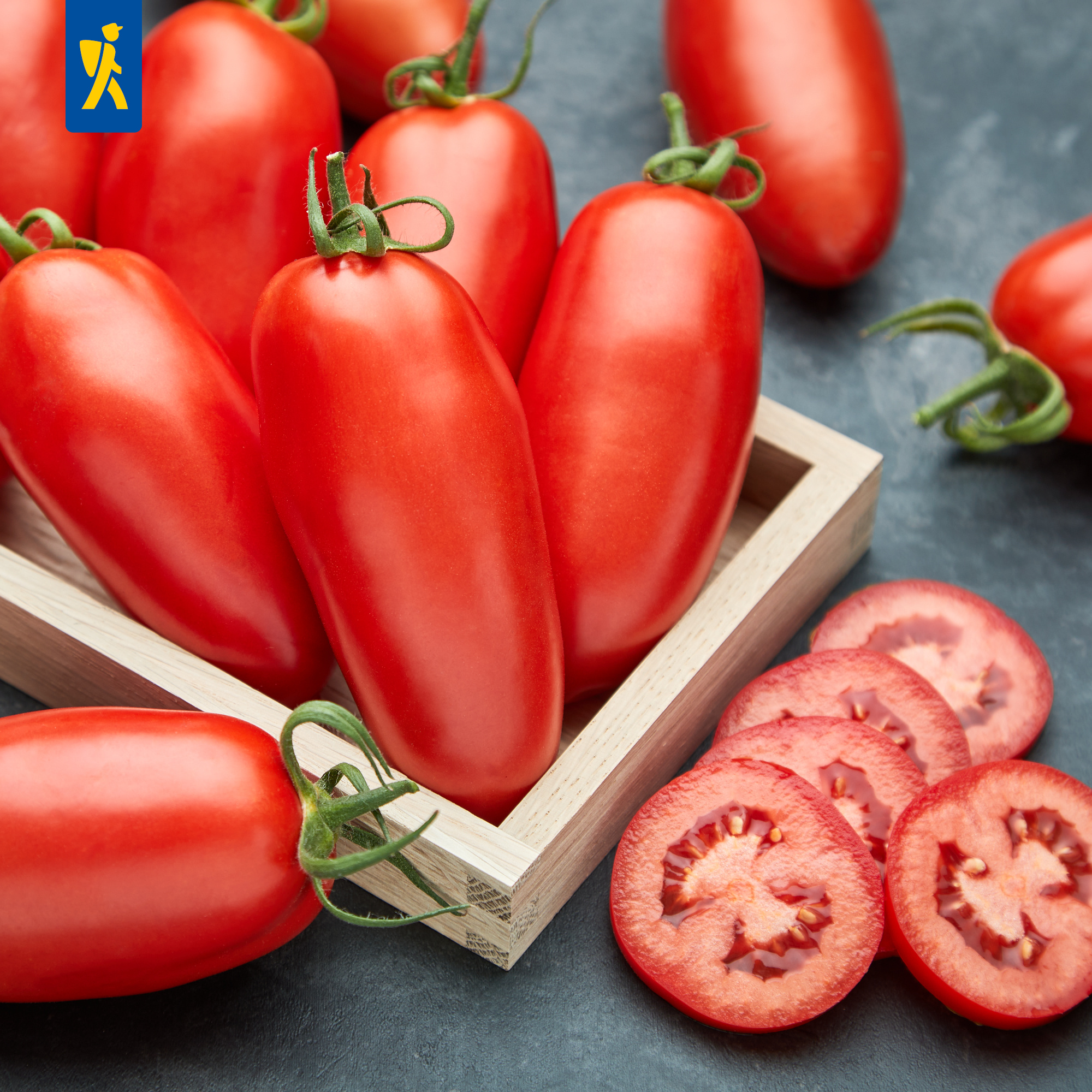 Rote Tomaten in Holzkiste mit einigen Tomatenstücken auf dunklem Hintergrund.