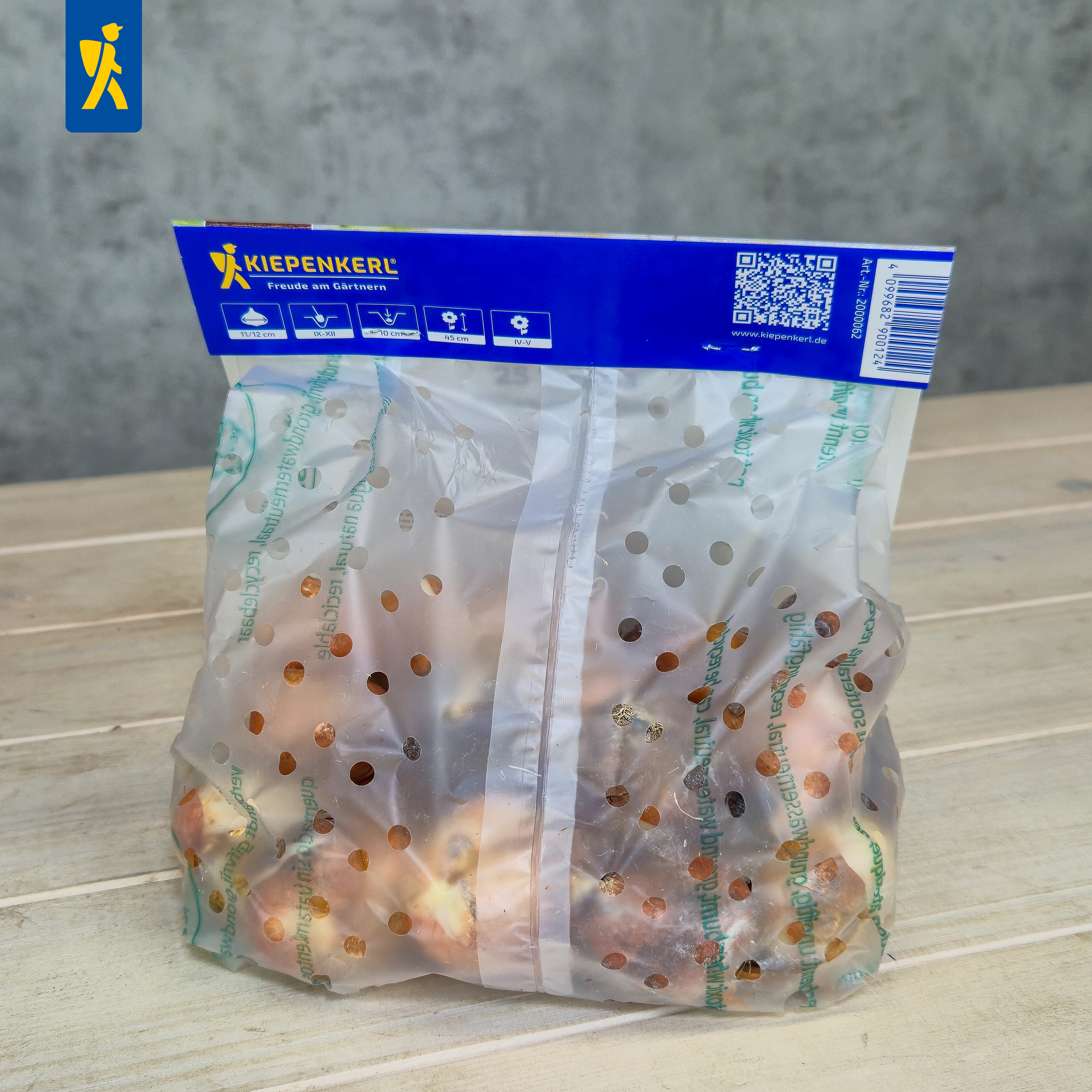 Perforierte Kunststoffverpackung mit Obst auf Holzoberfläche vor grauer Wand.
