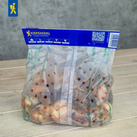 Perforierte Kunststoffverpackung mit Obst auf Holzoberfläche vor grauer Wand.