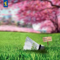 Badmintonschläger liegt auf grünem Rasen neben Schild mit Aufschrift Mein Paradiesrasen, im Hintergrund blühende Bäume.